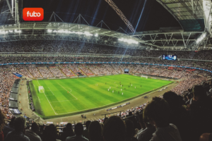 Fubo e Hulu + Live TV anunciam primeira sinergia pós-fusão. Imagem do estádio de futebol lotado durante partida ao vivo, destacando transmissão esportiva por streaming.
